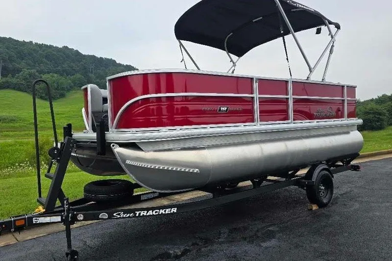 The Image of 2027 Sun Tracker Party Barge 18 DLX pontoon boat on trailer, red exterior, parked outdoors. - 0