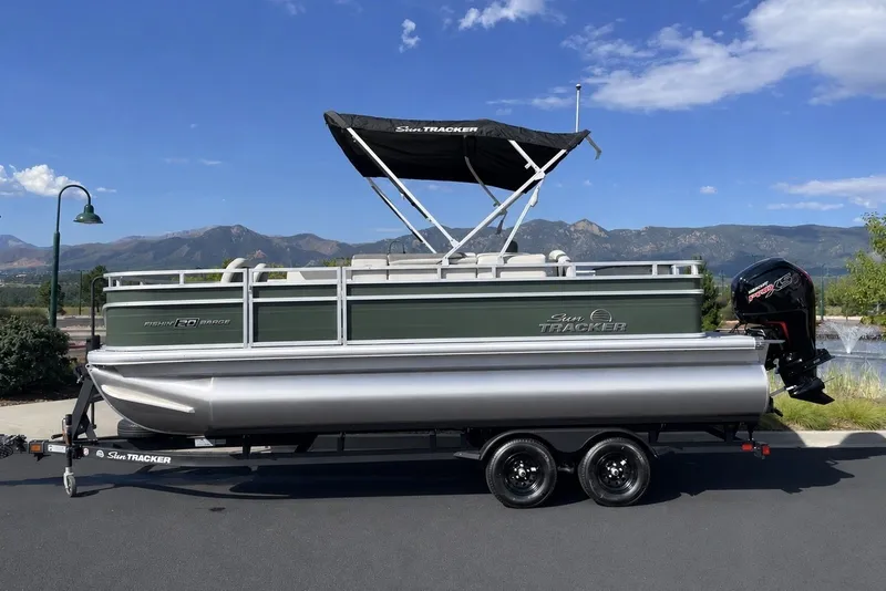 The Image of 2027 Sun Tracker Fishin' Barge 20 DLX pontoon boat on trailer, scenic mountain backdrop. - 0