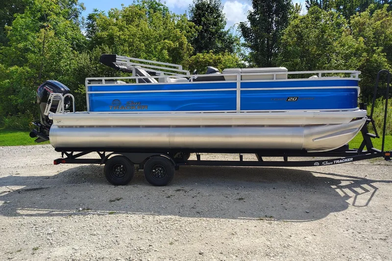 The Image of 2027 Sun Tracker Fishin' Barge 20 DLX pontoon boat on trailer, parked outdoors. - 0