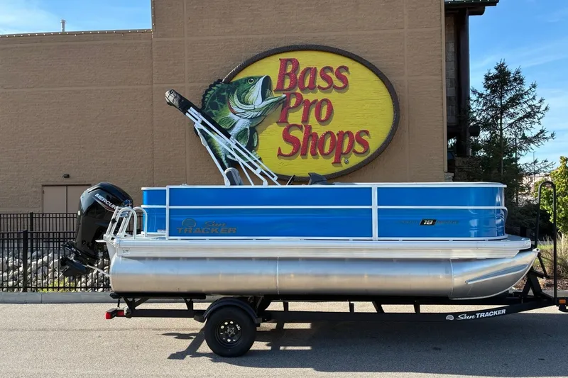 The Image of A Sun Tracker Party Barge 18 DLX pontoon boat on a trailer in front of a Bass Pro Shops building. - 0