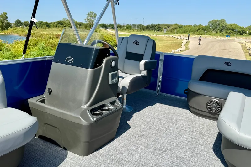 Slide: The Image of 2027 Sun Tracker Party Barge 16 DLX interior with helm and seating, near scenic waterway. - 13