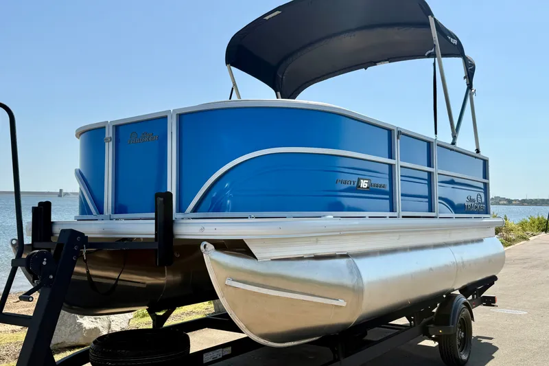 Slide: The Image of 2027 Sun Tracker Party Barge 16 DLX pontoon boat on trailer by the water. - 16