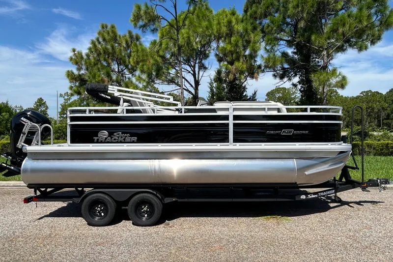 The Image of 2027 Sun Tracker Fishin' Barge 20 DLX pontoon boat on trailer, parked outdoors. - 0