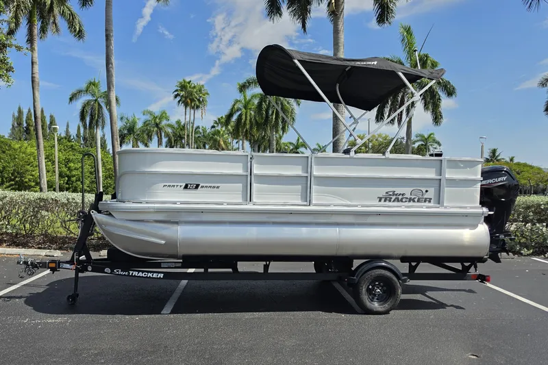 The Image of 2027 Sun Tracker Party Barge 18 DLX pontoon boat parked under palm trees. - 0