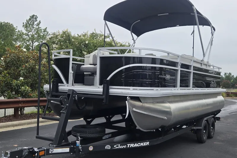 The Image of 2027 Sun Tracker Fishin' Barge 20 DLX pontoon boat on trailer, parked outdoors. - 0