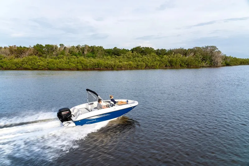 Slide: The Image of 2027 Bayliner 160 Element boat cruising on a serene lake with lush green shoreline. - 2