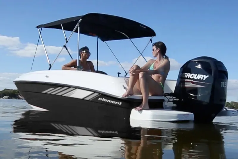 Slide: The Image of 2027 Bayliner Element E18 boat on water with two people, featuring a Mercury engine. - 7