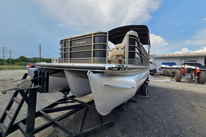 Slide: The Image of 2013 Sanpan 2500 FE pontoon boat on trailer, parked outdoors under a cloudy sky. - 2