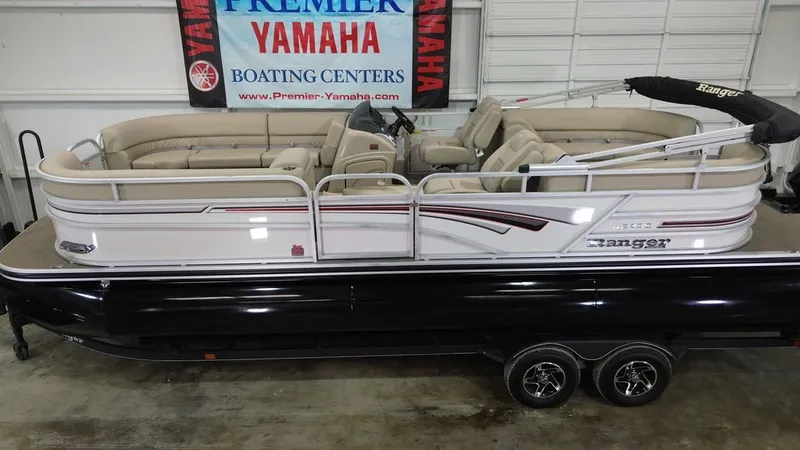 The Image of A 2023 Ranger RP243C pontoon boat in a showroom, featuring beige seating and a black hull. - 1
