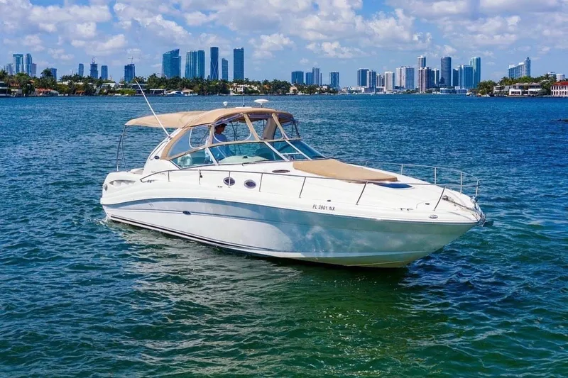 The Image of 2003 Sea Ray 340 Sundancer yacht cruising on a sunny day with city skyline backdrop. - 0