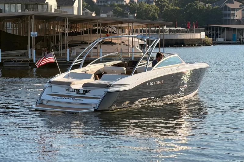 Slide: The Image of 2010 Cobalt 296 boat cruising on a sunny lake near docks, American flag waving. - 2