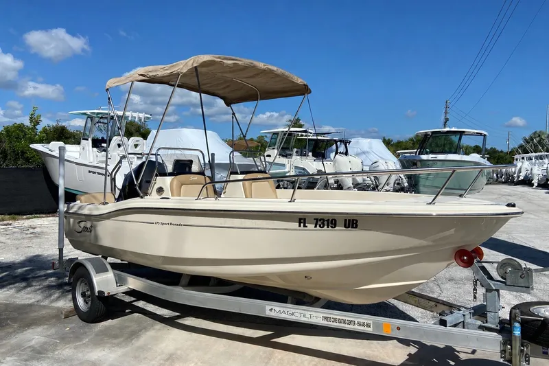 Slide: The Image of 2021 Scout 175 Sport Dorado boat on trailer, parked outdoors under clear blue sky. - 2