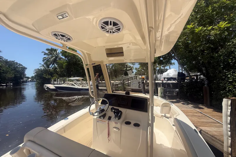 Slide: The Image of 2027 Scout 220 XSF boat interior with steering wheel, docked near lush greenery. - 14