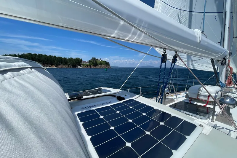 Slide: The Image of Sailboat with solar panels on deck, cruising near a forested island under clear blue skies. - 12