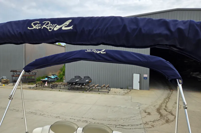 Slide: The Image of 2006 Sea Ray 240 Sundancer with blue canopy, parked near a metal building. - 58
