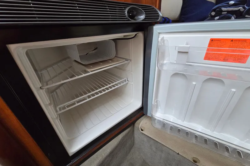 Slide: The Image of Open refrigerator inside 2006 Sea Ray 240 Sundancer boat, showing empty shelves and door storage. - 54