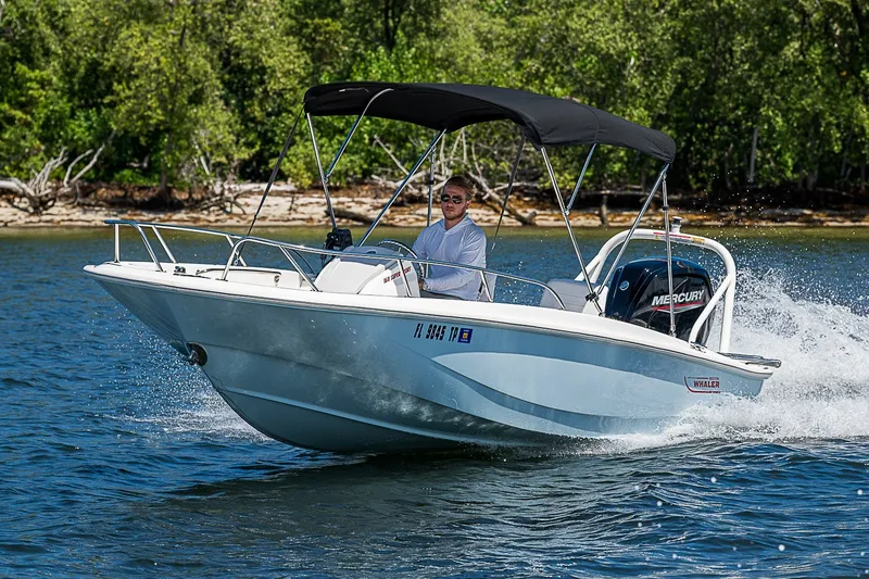 Slide: The Image of 2022 Boston Whaler 160 Super Sport cruising on a lake with lush green shoreline. - 1