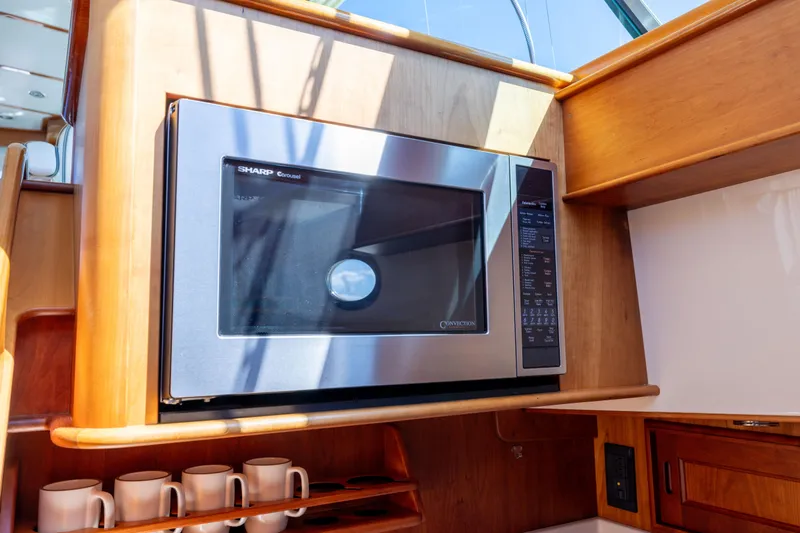 Slide: The Image of Microwave in 2014 Hinckley Talaria 48 Flybridge yacht kitchen, with wooden cabinetry and mugs. - 35