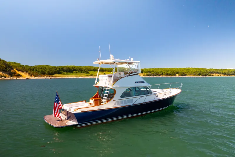 Slide: The Image of 2014 Hinckley Talaria 48 Flybridge yacht on serene water with scenic shoreline backdrop. - 79