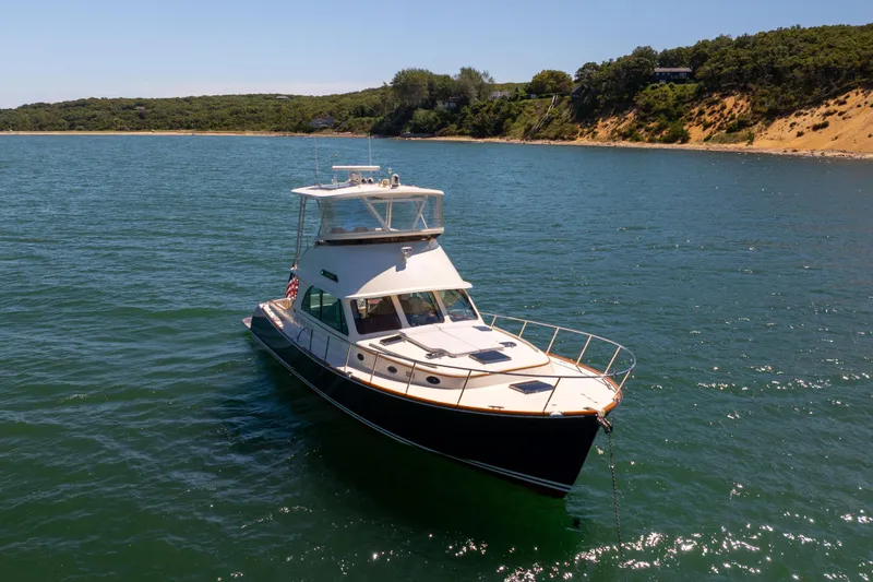 Slide: The Image of 2014 Hinckley Talaria 48 Flybridge yacht on serene water near a wooded shoreline. - 78