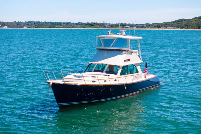 Slide: The Image of 2014 Hinckley Talaria 48 Flybridge yacht on clear blue water, scenic coastal backdrop. - 76