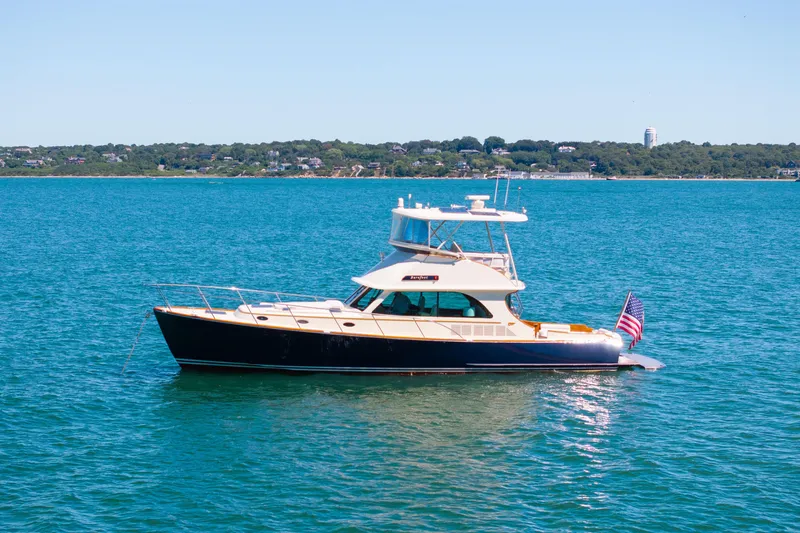 Slide: The Image of 2014 Hinckley Talaria 48 Flybridge yacht on serene blue water, distant shoreline view. - 77