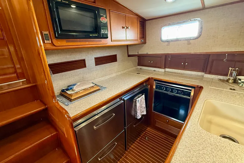 Slide: The Image of 2003 Grand Banks 49 Eastbay HX yacht kitchen with microwave, stove, and wooden cabinetry. - 53