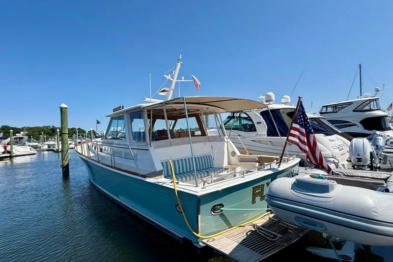 Slide: The Image of 2003 Grand Banks 49 Eastbay HX yacht docked at marina, featuring American flag and clear blue sky. - 32