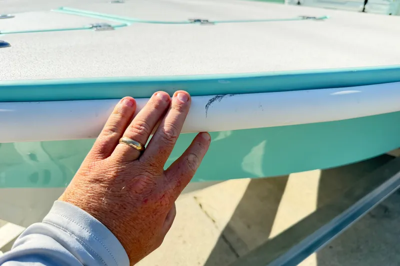 Slide: The Image of Hand touching the edge of a 2023 Egret 21 Moccasin boat, showing minor scuff marks. - 26