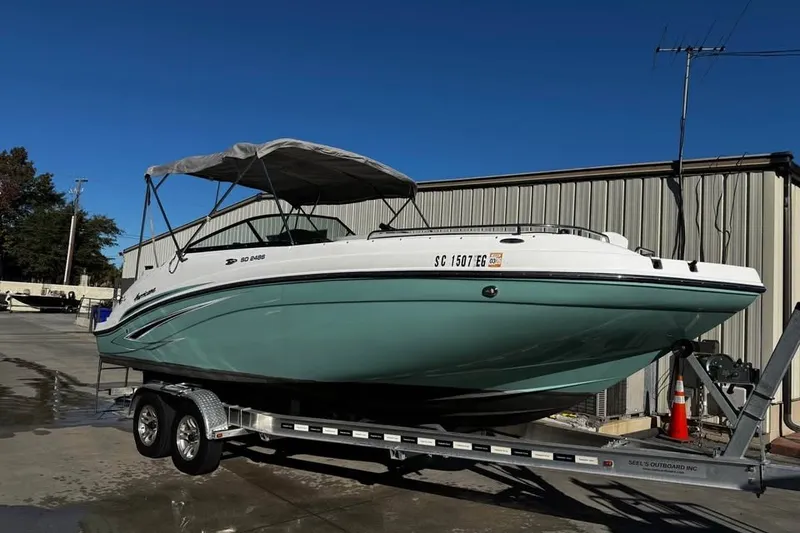 The Image of 2024 Hurricane SunDeck 2486 OB boat on trailer, parked outdoors under clear blue sky. - 1