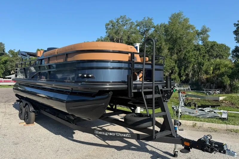 Slide: The Image of 2027 Ranger 220FC pontoon boat on trailer, parked outdoors with trees in background. - 1