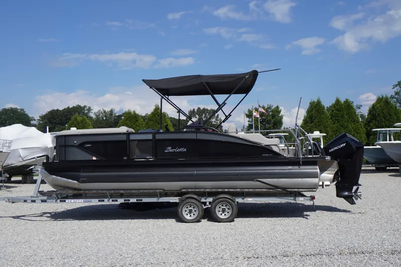 The Image of 2024 Barletta Cabrio 22UC pontoon boat on trailer, black exterior, sunny day. - 0