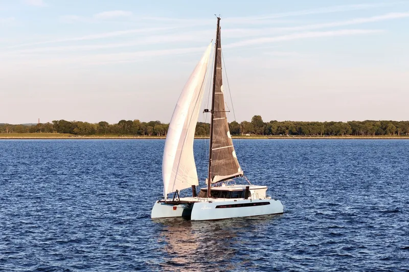 Slide: The Image of 2022 Balance 482 catamaran sailing on a calm blue sea near a forested shoreline. - 3
