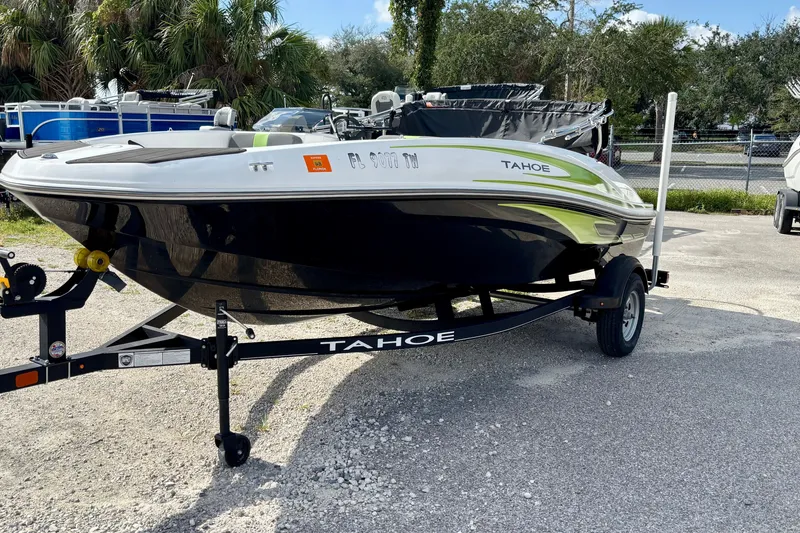 Slide: The Image of 2024 Tahoe T16 boat on trailer, parked outdoors with trees in background. - 2