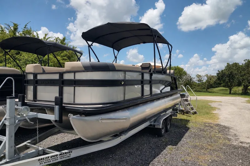 The Image of 2027 Sylvan L3 DLZ pontoon boat on trailer under blue sky. - 0