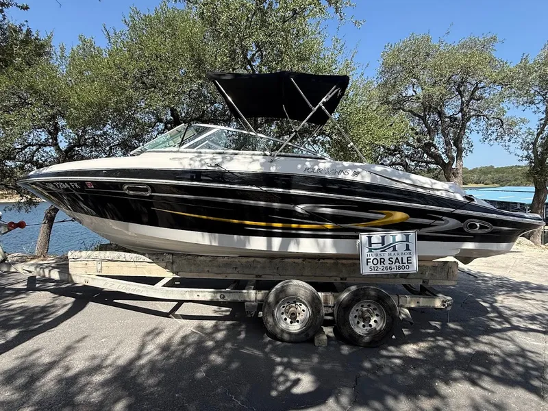 The Image of A 2006 Four Winns 240 Horizon on a trailer, surrounded by trees with a lake in the background. - 0