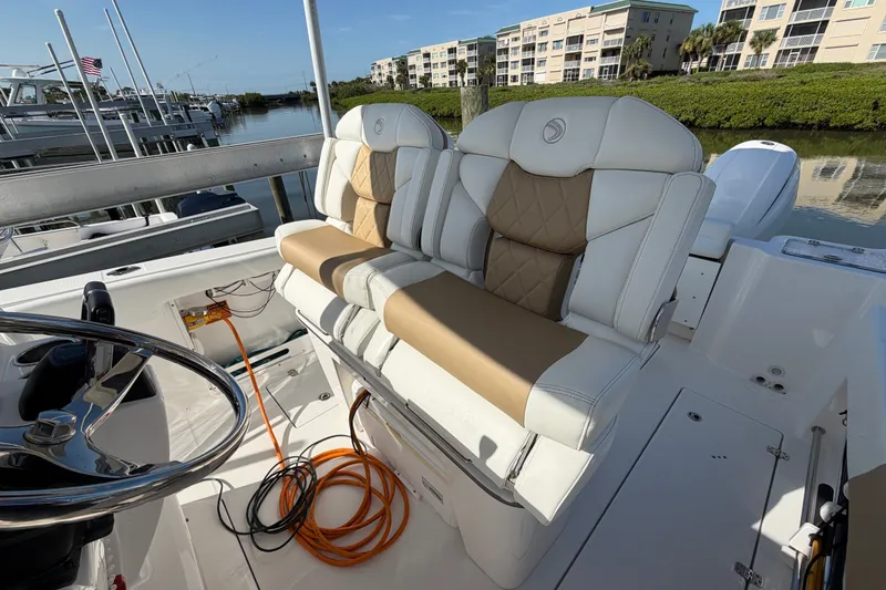 Slide: The Image of 2020 Edgewater 262CC boat interior with cushioned seating and steering wheel, docked near buildings. - 7