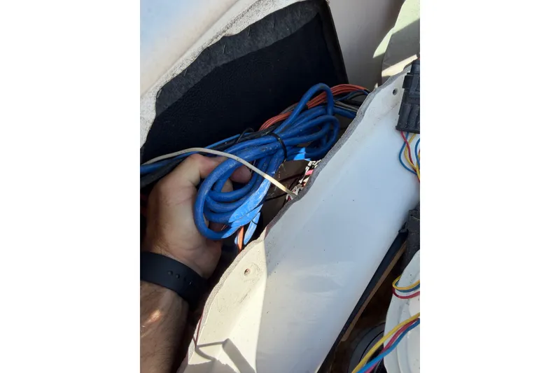 Slide: The Image of Hand holding blue cables inside a 2003 Sea Ray 240 Sundeck boat compartment. - 10