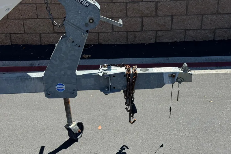 Slide: The Image of Trailer hitch of a 2022 Yamaha Boats 212S on pavement, featuring chains and a wheel. - 30