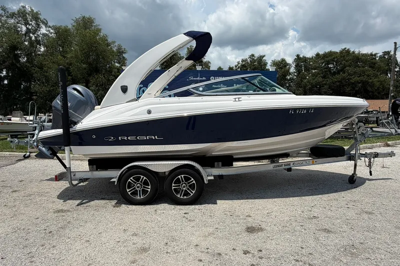 The Image of 2018 Regal 2100 boat on trailer, parked outdoors under cloudy sky. - 0