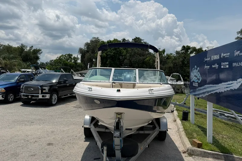 Slide: The Image of 2018 Regal 2100 boat on trailer in parking lot, surrounded by vehicles and signage. - 21
