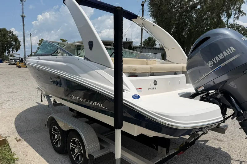 Slide: The Image of 2018 Regal 2100 boat on trailer with Yamaha outboard motor, parked outdoors. - 19