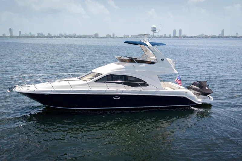 The Image of 2006 Sea Ray 44 Sedan Bridge yacht on calm water with city skyline in background. - 1
