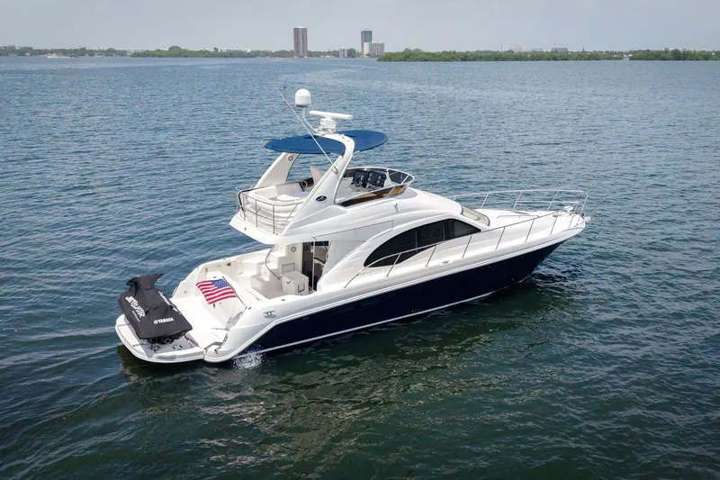 Slide: The Image of 2006 Sea Ray 44 Sedan Bridge yacht cruising on open water with city skyline backdrop. - 5