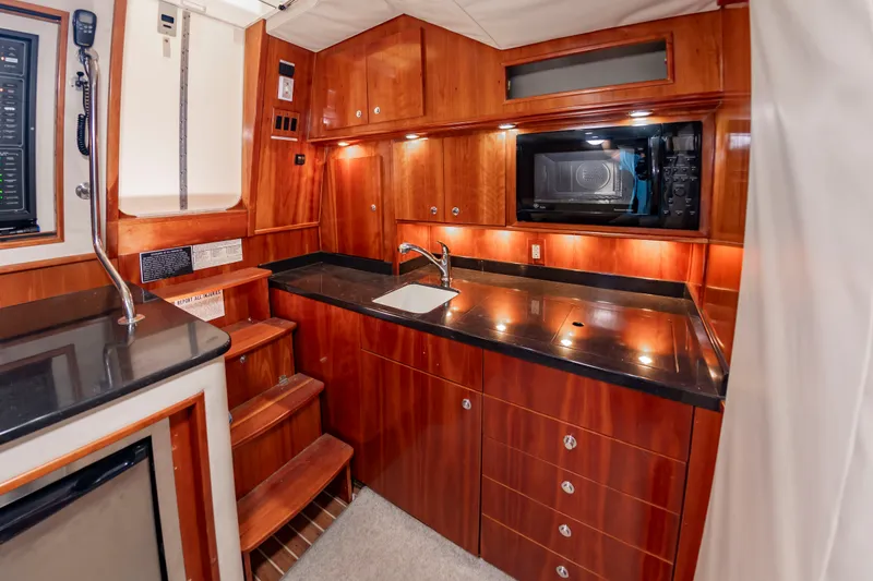 Slide: The Image of The 2004 Albemarle 410 Express Fisherman galley features wooden cabinets, a sink, and a microwave. - 33