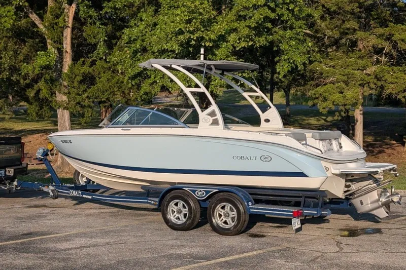 Slide: The Image of 2020 Cobalt 220S boat on trailer, parked outdoors with trees in background. - 2
