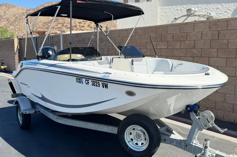 Slide: The Image of 2023 Bayliner Element M17 boat on trailer, parked outdoors with bimini top. - 1