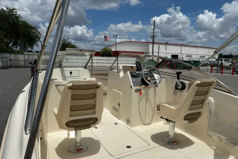 Slide: The Image of 2023 Scout 210 Dorado boat interior with dual seats and steering wheel under a cloudy sky. - 12