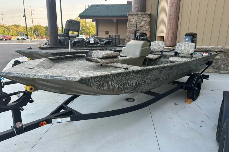The Image of 2027 Tracker Grizzly 1754 SC boat on trailer, camo design, parked outdoors. - 0