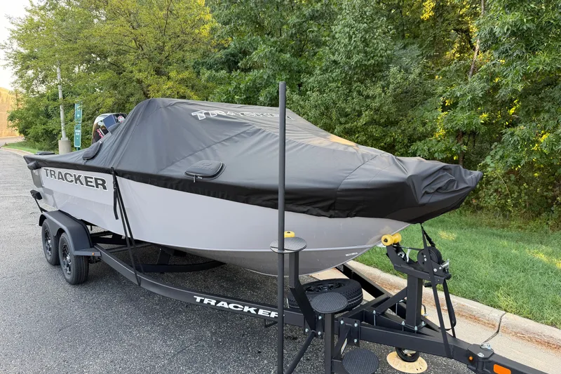 Slide: The Image of 2027 Tracker Targa V-18 Combo boat covered on trailer, parked near trees. - 22